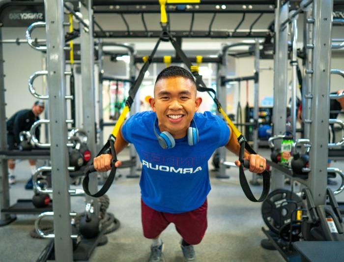 A student in the gym on a trx machine leaning in and smiling